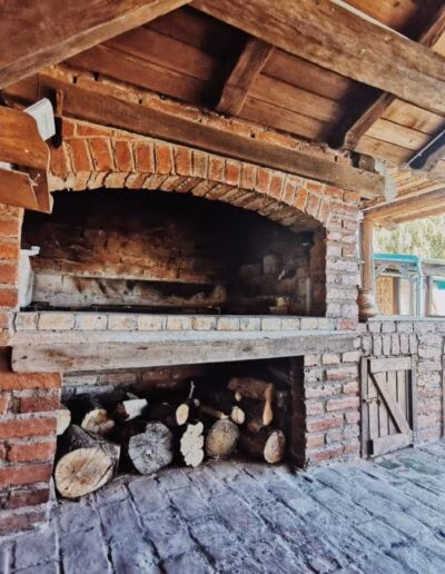 Vanjski kamin od crvene cigle s drvenom krovnom konstrukcijom i spremištem za drva ispod, u dvorištu kuće za odmor.
