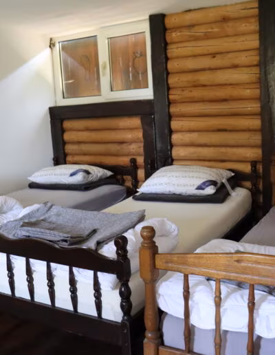 Soba s tri drvena kreveta postavljena uz zid od drvenih trupaca i malim prozorom.