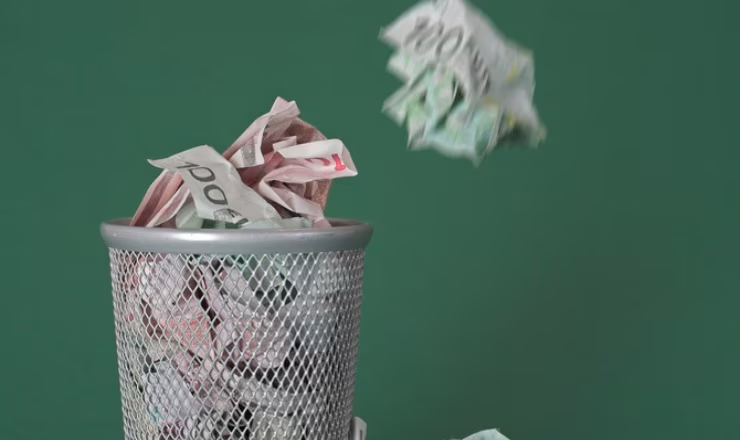 Photo of a waste basket full of money - some bills are just dropped in the basket.