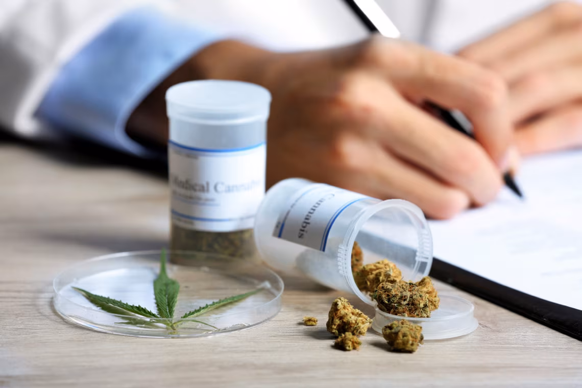 Doctor writing on prescription blank and bottle with medical cannabis on table close up