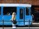 woman in black leather backpack standing beside blue and white train during daytime