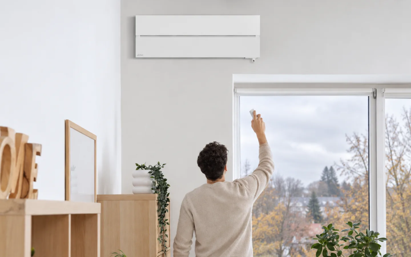 Moški z daljincem upravlja klimatsko napravo Mitsubishi Electric na steni v svetlem dnevnem prostoru