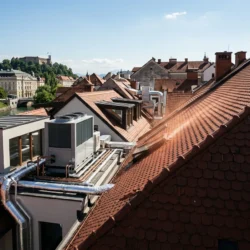 Moderna notranja enota klimatske naprave, nameščena na vertikalno steno pod poševnim stropom v svetli mansardi.