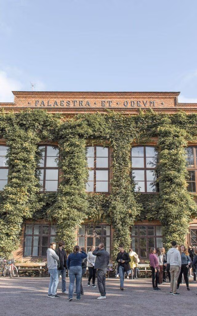 a group of people standing outside a building with ivy on it